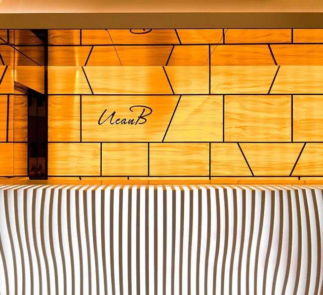 UcanB reception with backlit wood panels, the script UcanB logo and a white wave-patterned counter
